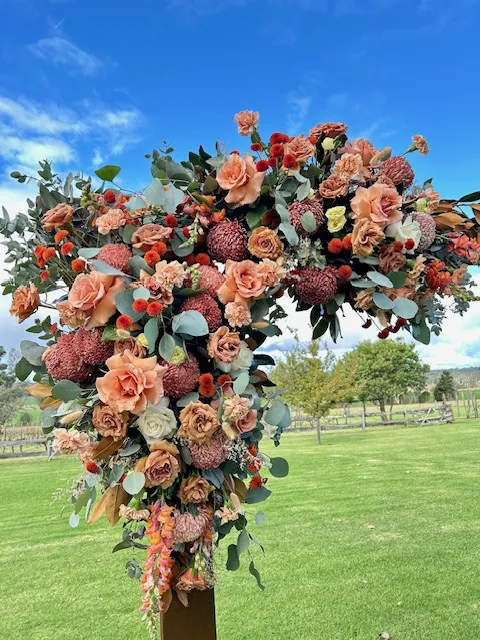 Close view of pink, coral and cream flowers with greenery on a timber wedding arbour at Belgenny Farm.