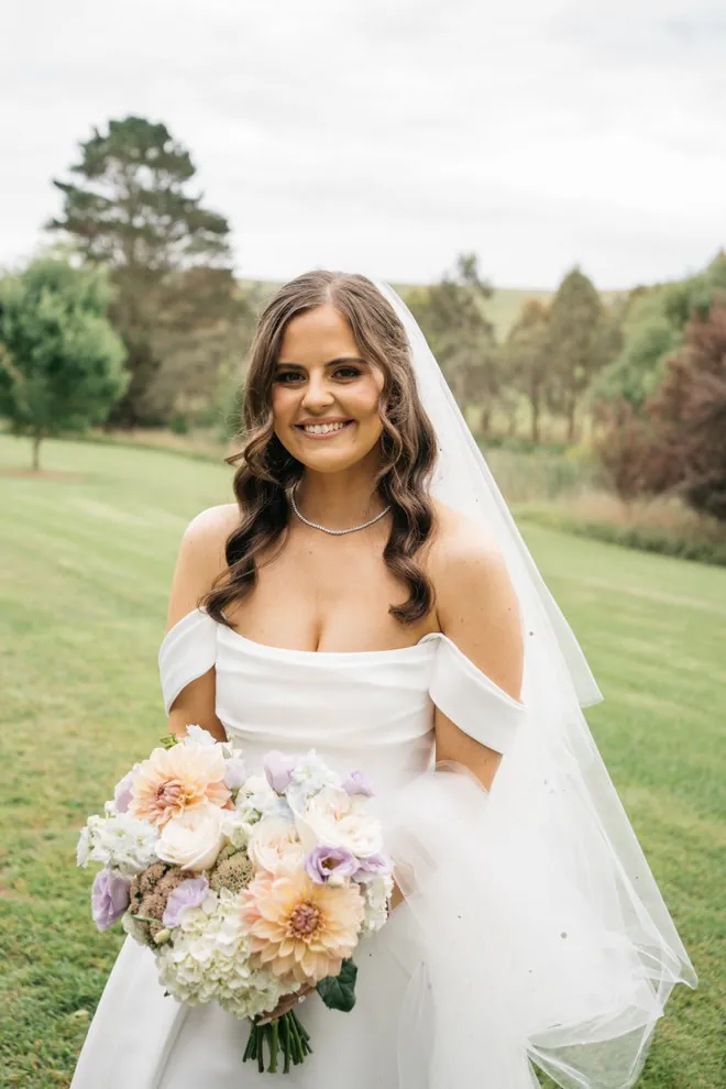 Cassie holding a pastel bouquet with peach, cream and lilac flowers on a garden lawn.
