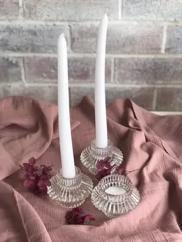 Three clear crystal candle holders with white taper candles displayed on pink fabric.