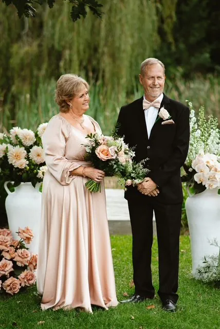 Floyd and his mum holding flowers beside pastel floral arrangements in a garden.