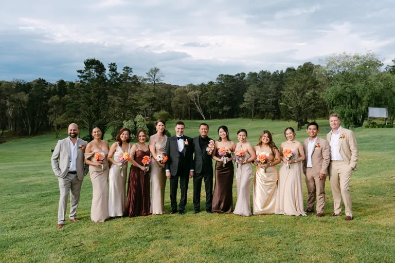 James and David with their wedding party holding colourful bouquets on a garden lawn.