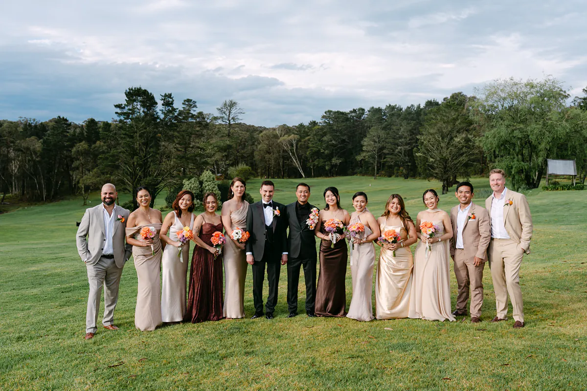 James and David with their wedding party holding colourful bouquets on a garden lawn.