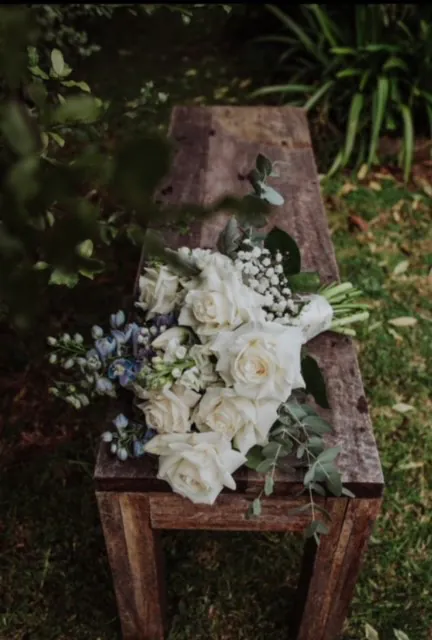 White bridal bouquet with trailing ribbons resting on a timber garden chair.