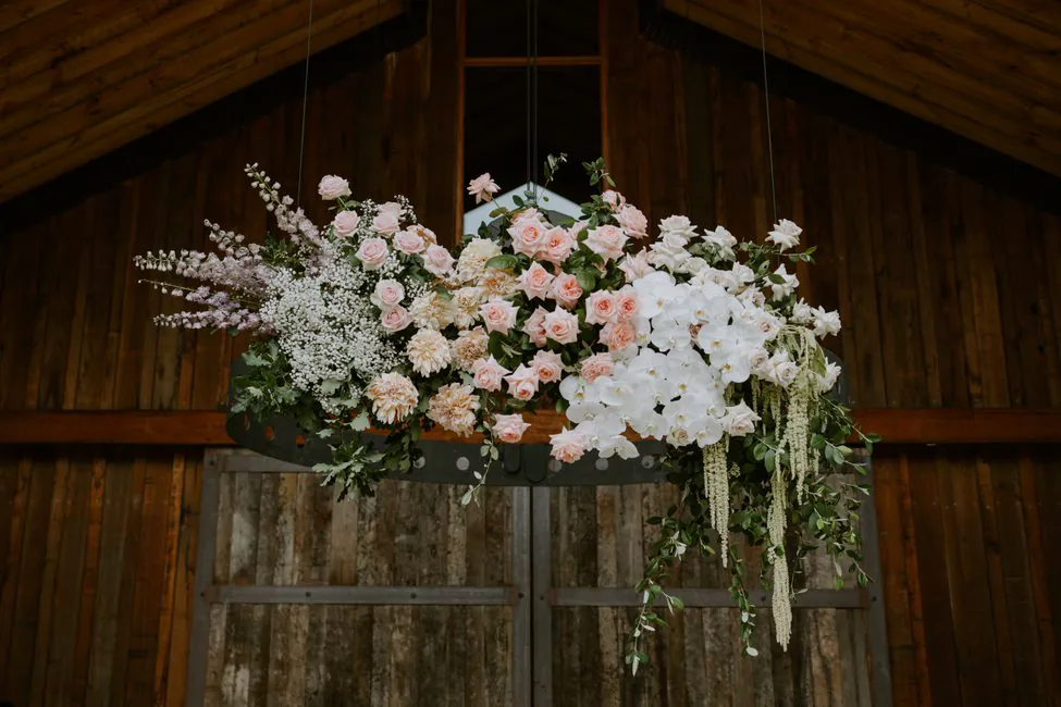 Suspended wedding floral arrangement with pink and white flowers and trailing greenery in a timber venue.