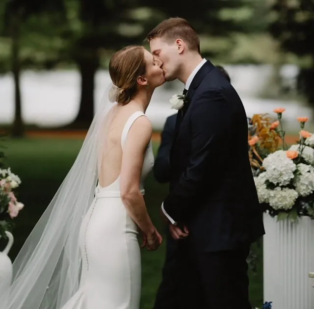 Olivia and Fred kissing beside white and orange wedding flowers in a garden.