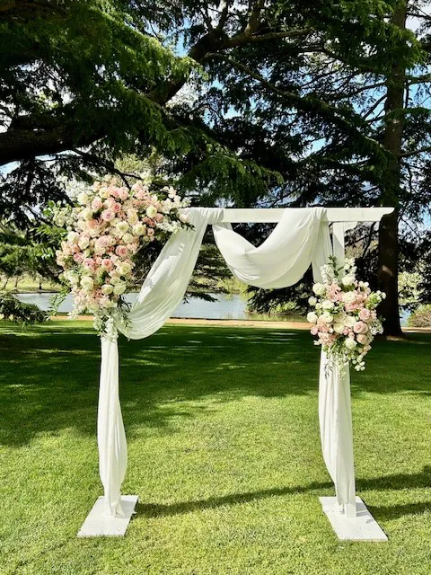 White wedding arbour decorated with pastel flowers and soft fabric draping on a lawn.