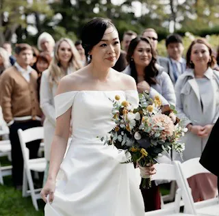 Samantha holding a pastel bouquet with cream and peach flowers during her outdoor wedding ceremony.