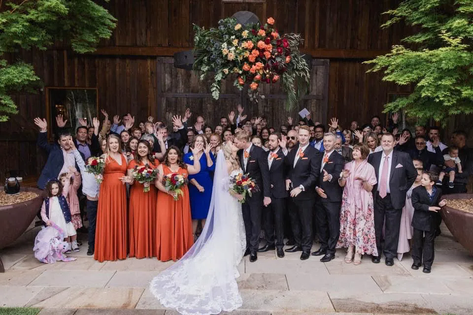 Wedding party beneath a vibrant floral installation styled by The Red Poppy Florist.