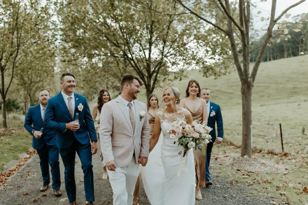Bride and groom walking with their wedding party and white bouquets along a garden path.