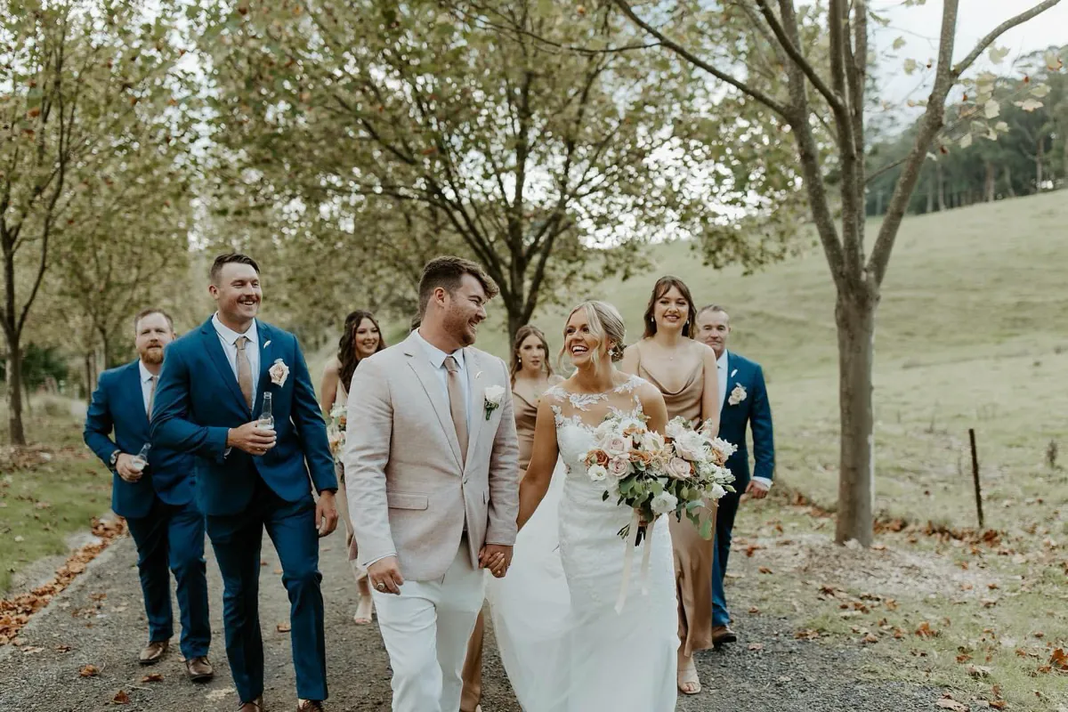 Wedding party carrying elegant white floral bouquets along a garden path, The Red Poppy Florist.