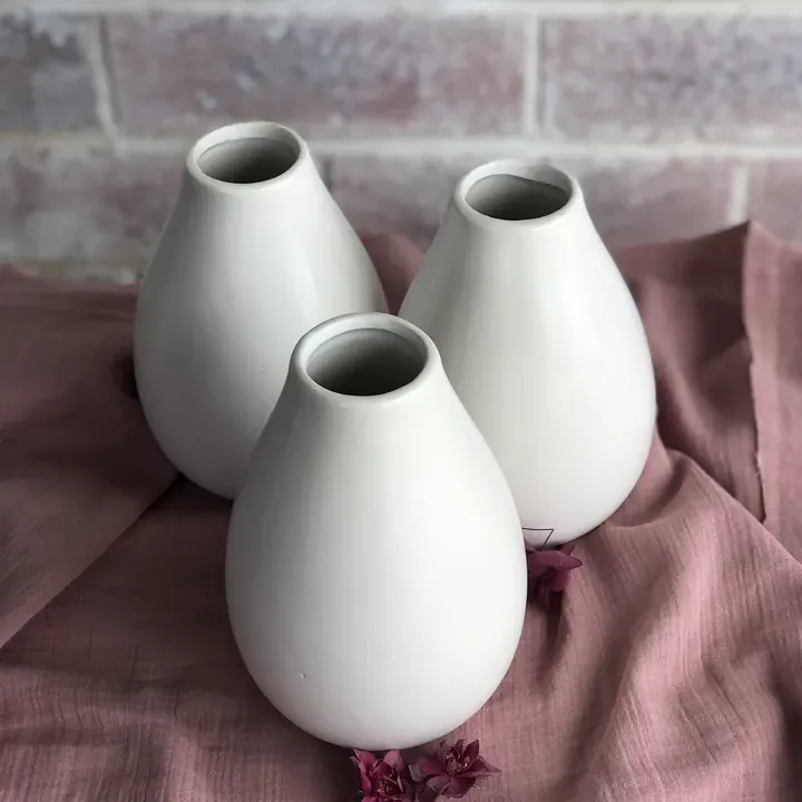 Three rounded white ceramic vases displayed on dusty pink fabric.